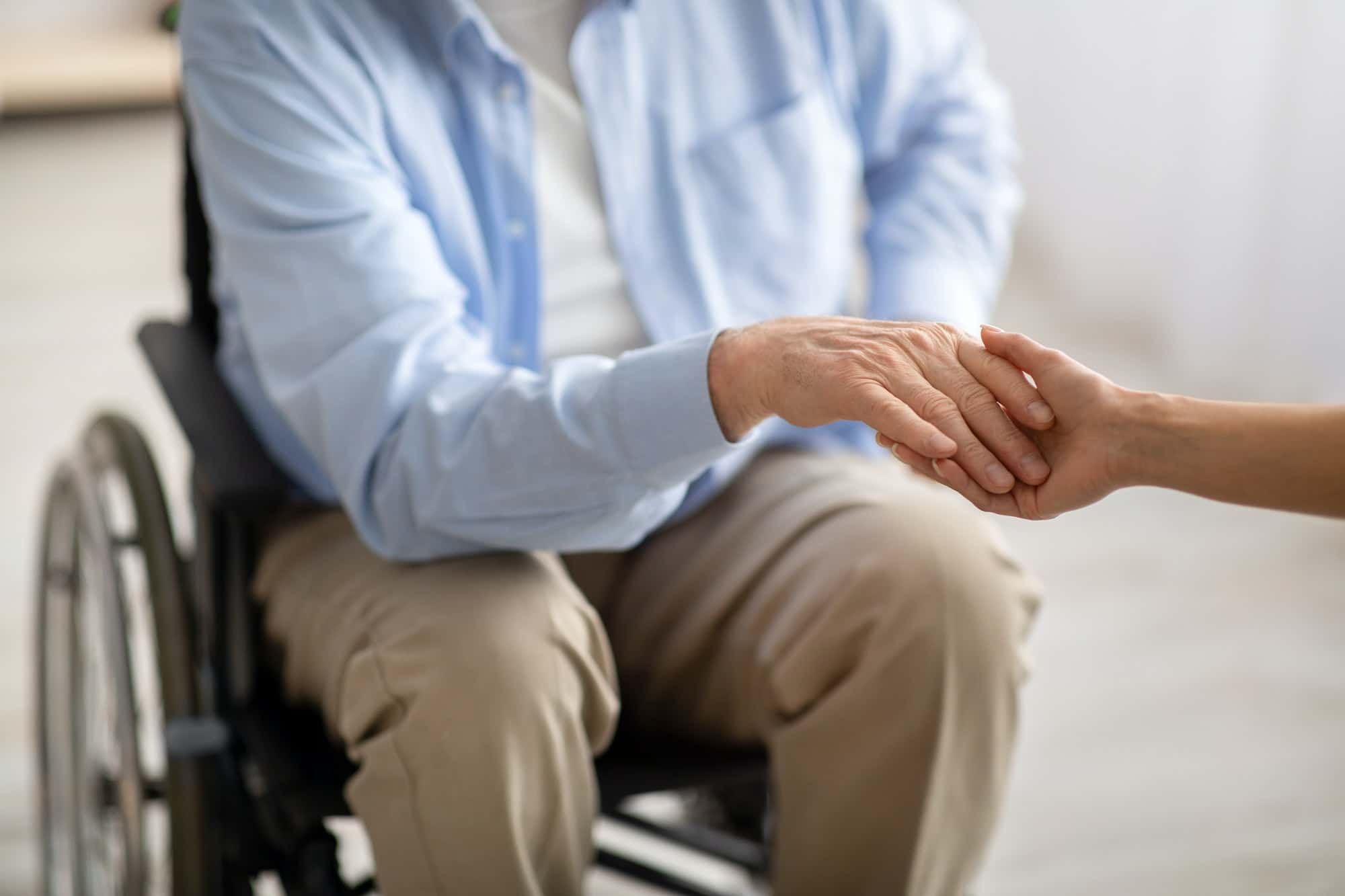 Elderly disabled people support. Young female holding hand of handicapped senior man in wheelchair