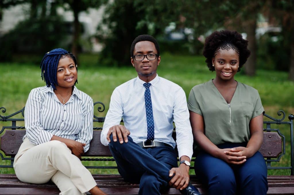 Group of three african american people posed at street of city sitting on the bench.