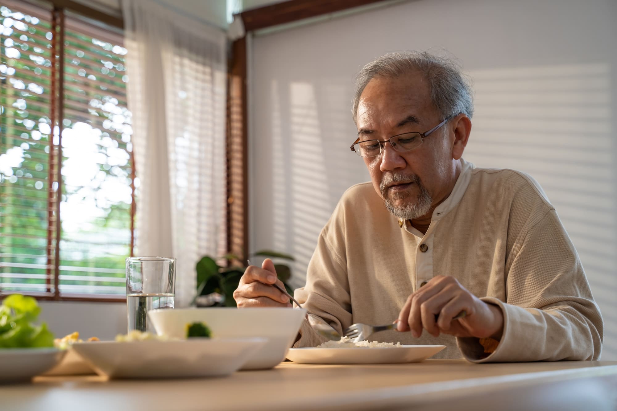 Unhappy Asian Senior older man sit alone, eat foods on table in house.